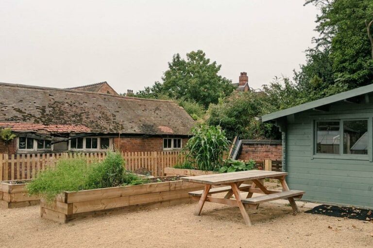 A fenced area which includes a raised bed planter, a picnic bench and a wooden cabin