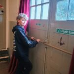 A young man stood holding the push bar of a door